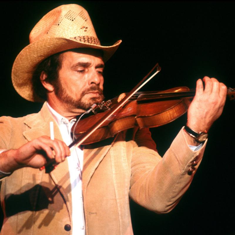 Country music legend Merle Haggard plays a fiddle in a cowboy hat