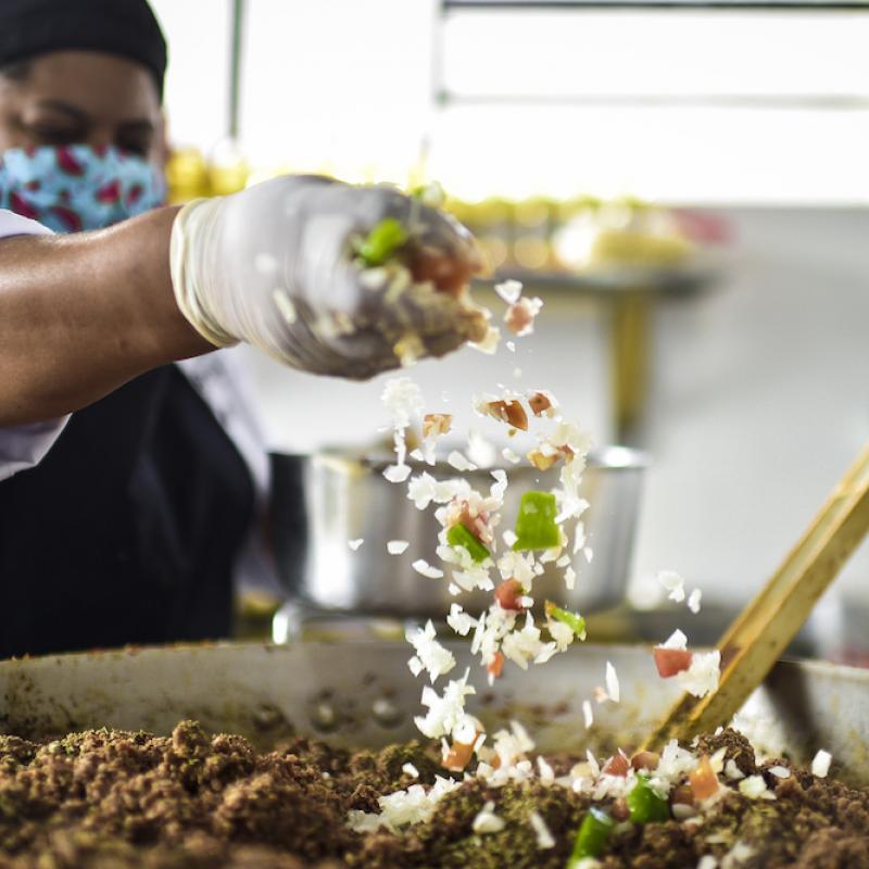 Woman sprinkles spice into a pan of meat while cooking.