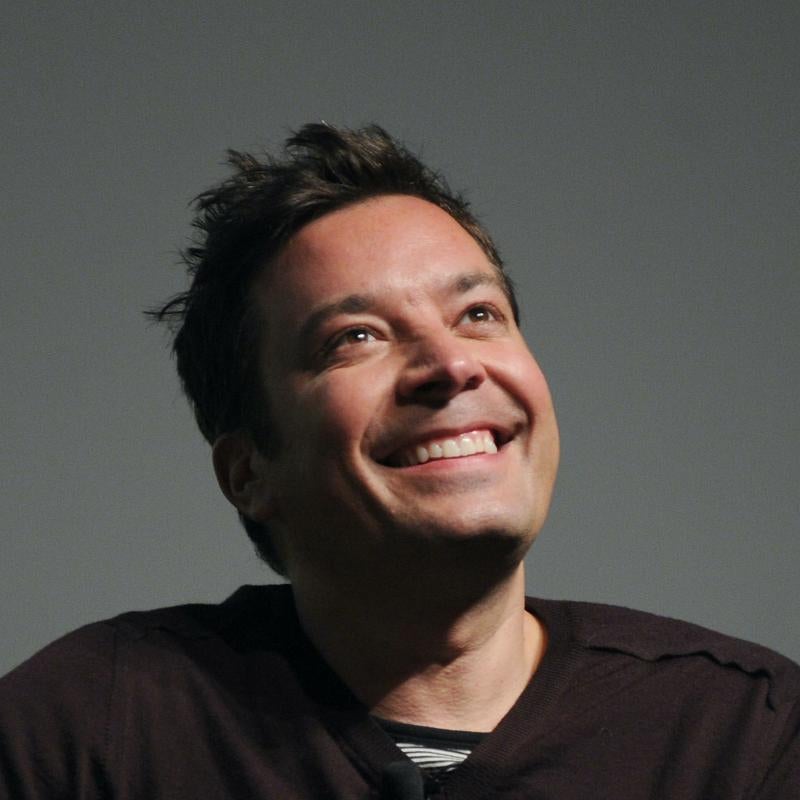 Comedian and talk show host Jimmy Fallon smiles and looks upwards against a gray background
