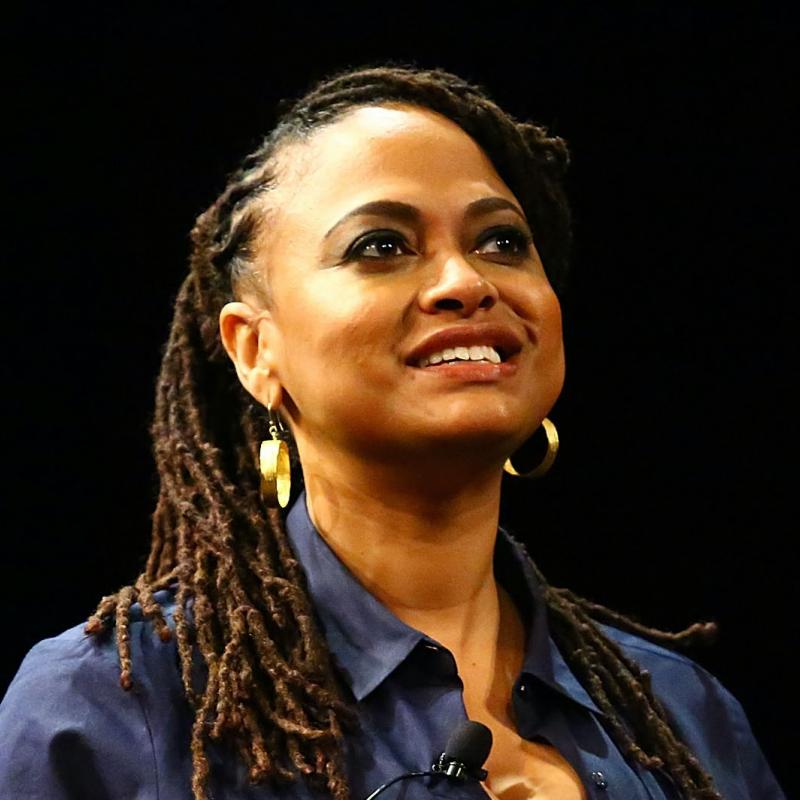 Film director Ava Duvernay smiles on stage against a black backdrop